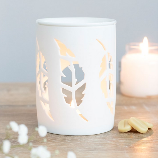 White candle holder with feather design on a wooden surface with a lit candle.