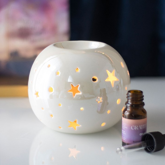 White ceramic diffuser with star designs on a white surface next to a bottle of essential oil.