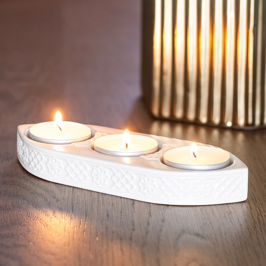 White ceramic candle holder with three lit candles on a wooden surface.