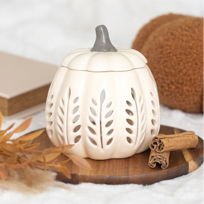 White pumpkin-shaped lantern with a gray top on a wooden surface with cinnamon sticks and leaves.