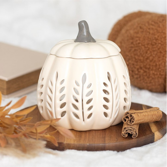White pumpkin-shaped lantern with a gray top on a wooden surface with cinnamon sticks and leaves.