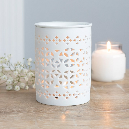 White ceramic lantern with cut-out design on a wooden surface with a lit candle inside.