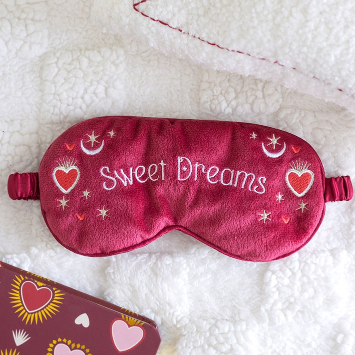 Red sleep mask with 'Sweet Dreams' text on a white fluffy surface