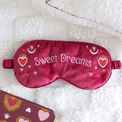 Red sleep mask with 'Sweet Dreams' text on a white fluffy surface