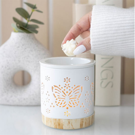 White wax warmer with butterfly design on a white surface, hand holding a candle.