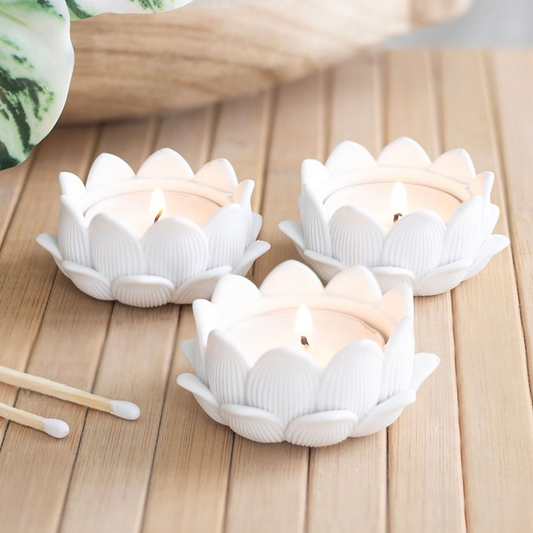 Three white lotus-shaped candle holders with candles on a wooden surface.