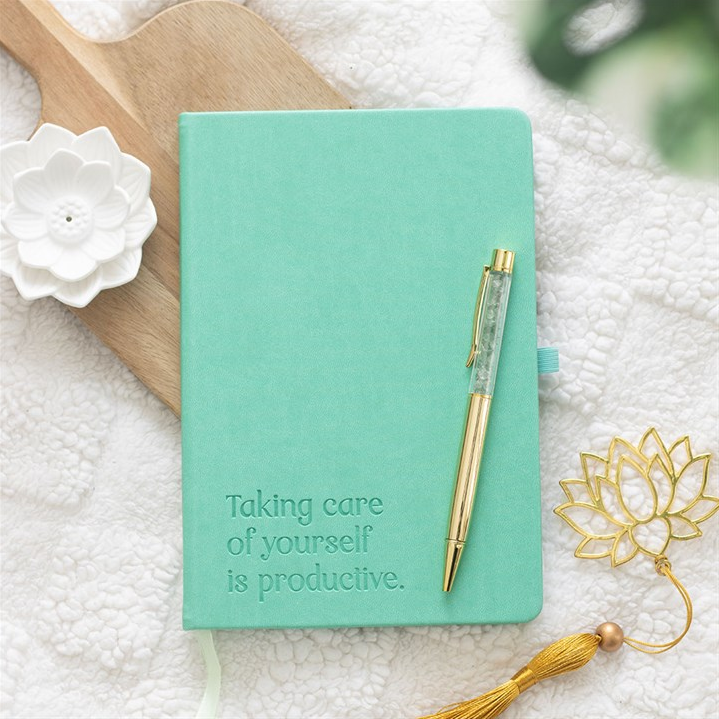 Mint green notebook with a pen on a textured surface with decorative elements.