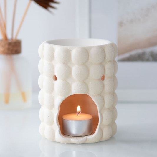 White textured candle holder with a lit candle inside on a light background