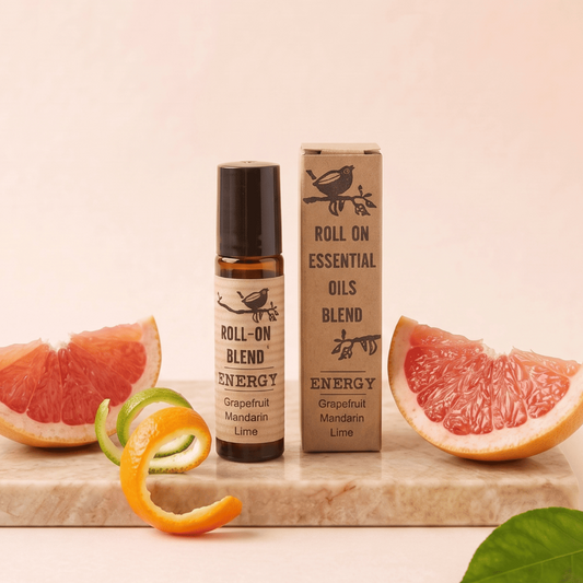 A roll-on oil blend bottle and its matching kraft paper box labeled 'Roll On Essential Oils Blend Energy Grapefruit Mandarin Lime,' styled on a marble slab with grapefruit slices, orange peel, and lime slices against a soft beige background.