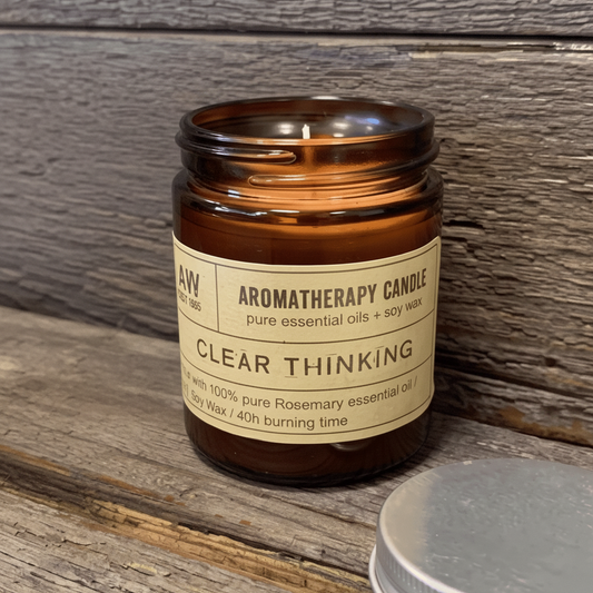 An amber glass jar candle labeled 'CLEAR THINKING' sits on a rustic wooden surface.