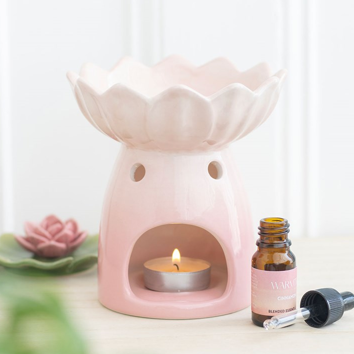 Pink ceramic oil burner with a lit candle and essential oil bottle on a white background