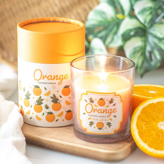 Orange-scented candle with packaging and sliced oranges on a white background