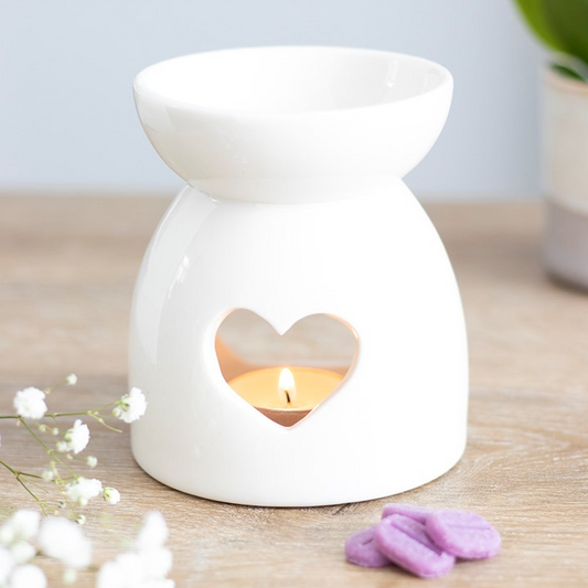 White ceramic oil burner with heart design on a wooden surface.