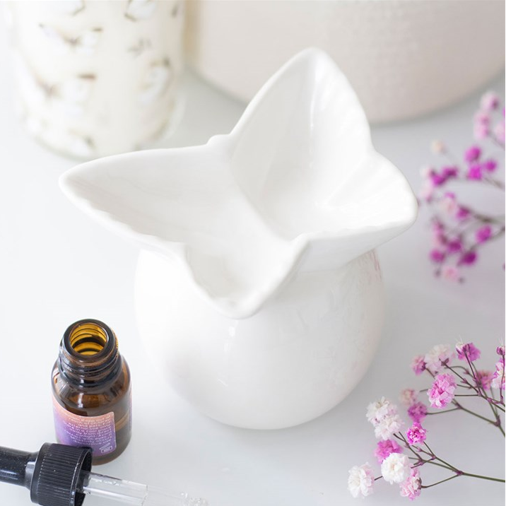 White ceramic star-shaped container with a small bottle and flowers on a light surface